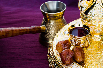 Still life with traditional golden arabic coffee set with dallah, coffee pot (jezva), cup and dates. Dark background. Horizontal photo