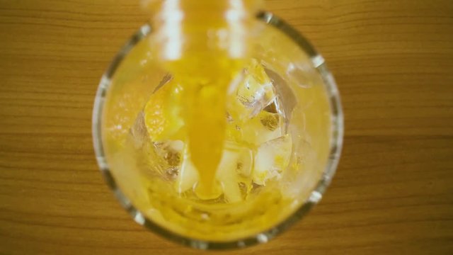 Slow mo. Orange drink from a bottle in a glass with ice and orange to pour top view