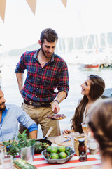 Man serving pan for friends at sea barbecue party