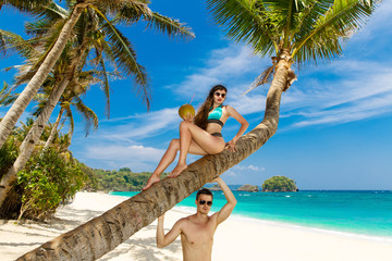 Young loving couple on a palm tree on a tropical beach. Tropical sky and sea in the background....