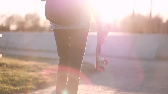 Young Guy Walking With a Skateboard in Hands, in the Sunset Time, in Denim Jacket and Black Jeans