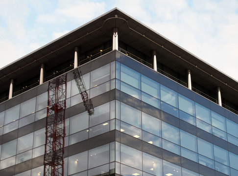 modern glass and black office building with reflection of a construction crane and blue sky
