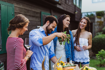 Man pouring olive oil into salad with girls at barbecue outdoors