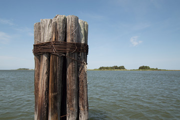 Bundle of weather pier poles in water with islands in the distance