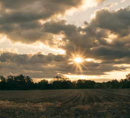 Plowed field with leading lines to sun in a cloudy sky