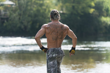 Fototapeta na wymiar Bodybuilder Flexing Muscles Outdoors In Nature