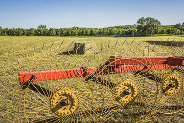 A hay rake in the foreground of a baled alfalfa field with a big square bale in the background on a sunny day.