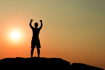 Silhouette of half naked confident man doing a winning pose against the sun on rocky ground
