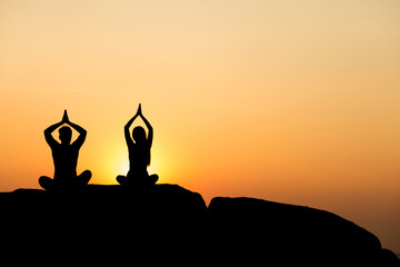 Silhouette of attractive confident half naked man and woman doing yoga on beach rock