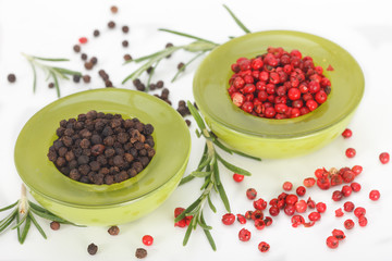 Black and red peppers in green bowls on white background
