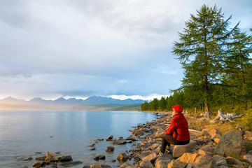 A woman looks at the lake Hovsgol in the sunset light. Peak Munku-Sardyk - near the center of the frame on the left. Eastern Sayan. Mongolia. 