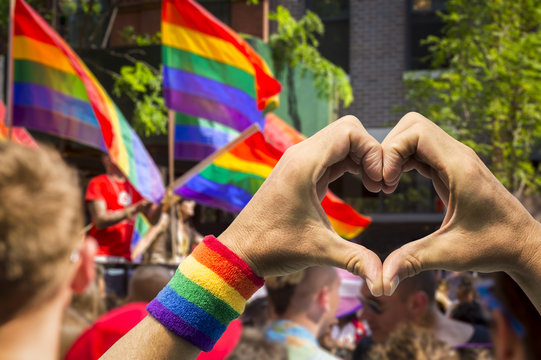 Supporting hands make heart sign and wave in front of a rainbow flags flying on a float of a summer gay pride parade