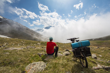 Traveler on a bicycle, summer, at the top of a mountain, panorama of mountains with clouds