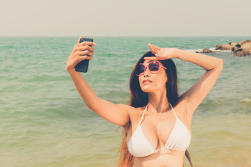 Beautiful attractive large breast asian bikini woman posing sexy portrait on beach smart phone selfie