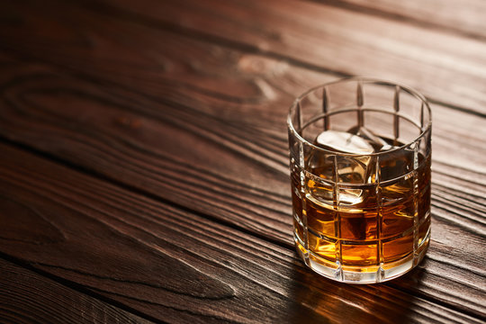 Glass of whiskey with ice cubes on wooden table