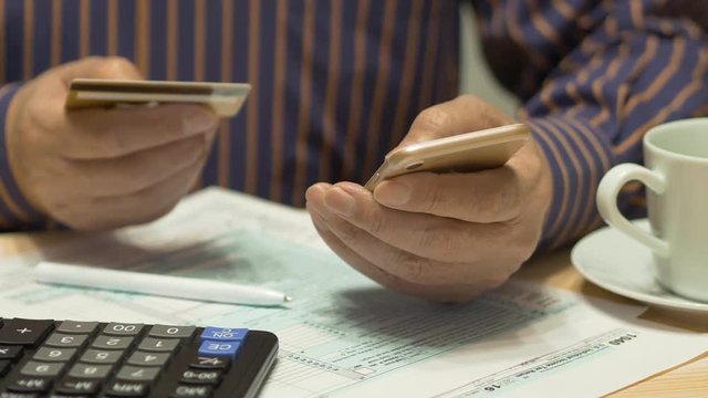 Elderly Man Text Messaging On Smartphone And Tax Form 1040, Credit Card