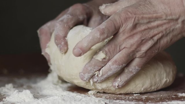Senior woman hands knead dough on a table in her home kitchen. Slow motion