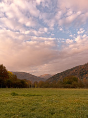 Naklejka na ściany i meble Autumn landscape at dawn with cloudy sky, meadow, mountain peak in the sunlight and forest. Caucasus. Russia. The Caucasian reserve. Cordon Guzeripl