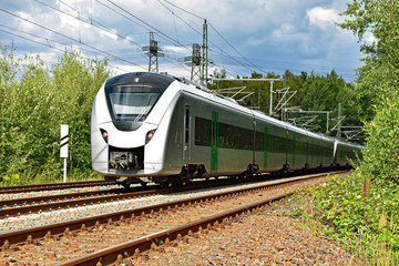 A modern electric regional train runs on a multi-lane track through natural surroundings