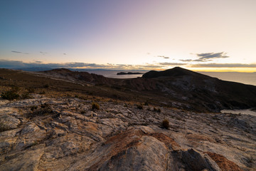 Sunset light on the Island of the Sun, Titicaca Lake, among the most scenic travel destination in Bolivia. Expansive panorama with glowing rocks in the foreground.