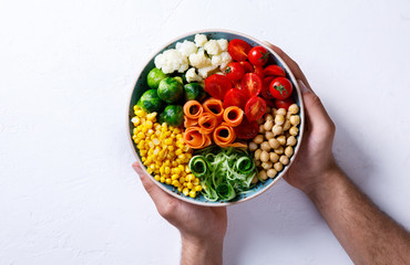 Raw mixed Vegetables and chickpeas on a white. Background Vegetarian Buddha Bowl in the Men's Hands. Food or Healthy diet Concept.Super Food.Copy space for Text. selective focus.
