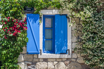  Window with blue shutters and blooming jasmine and bougainvillea plant on stone wall  at Alacati, Turkey