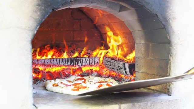 Pizza being baked in traditional wood burning pizza-bread oven in a restaurant.