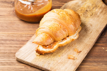 Fresh croissants with salted caramel on a brown wooden background, closeup, horizontal, selective focus
