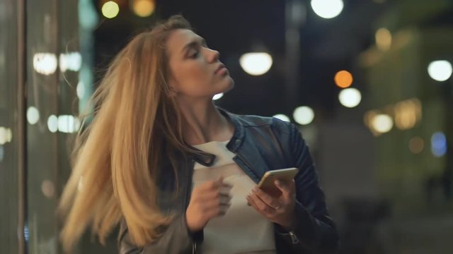Blonde young girl use mobile phone in city at night