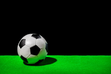 soccer ball on green grass over black background, concept of competitive sport