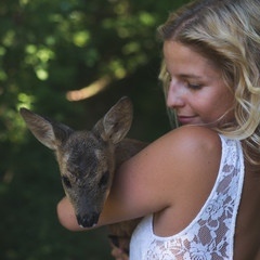 Beautiful woman in the forest with roe deer fawn. Animal protection concept.