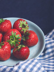 Closeup of fresh strawberries on an old blue vintage plate and checked kitchen cloth on dark navy background. Copy space.