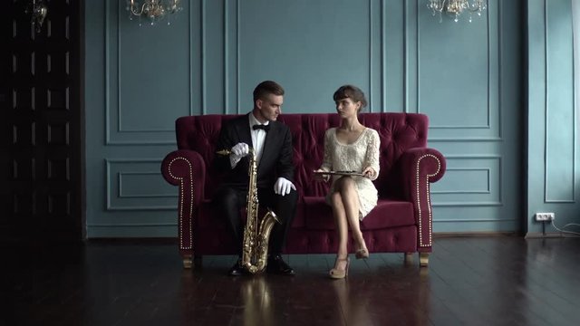 Musician and young woman sitting on a red sofa in the room. The end musical clip.