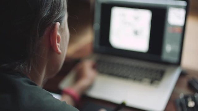 Woman designer working at a laptop with a graphics tablet. The view from behind shoulder, close-up