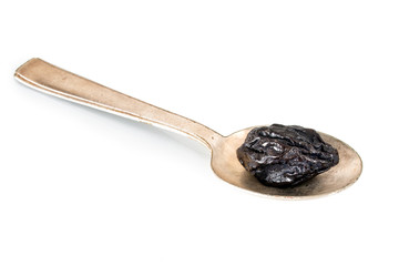 Prune, dried plum, on spoon on white. Healthy snack.