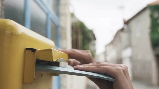 Woman is sending a blue letter into a yellow letterbox. Slow motion 120 fps
