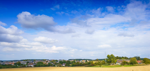 Panoramic shot of field with distant buildings and clouds, Belgium.
