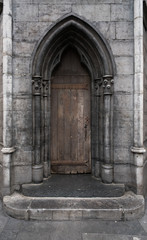 Closed wooden door with archway of church with stone walls, Belgium.