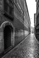 Fototapeta na wymiar View along narrow street of buildings and cobbles, black and white, Belgium.