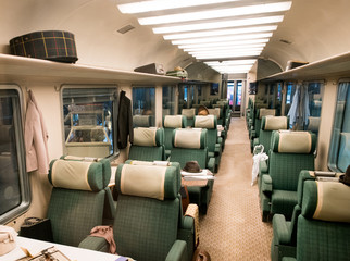 Empty green seats with cushions in train carriage, view along aisle.