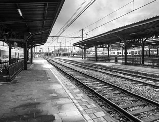 Obraz na płótnie Canvas Empty railway station platform with train tracks, black and white, Belgium.