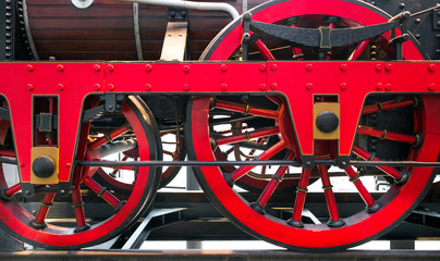 Close up of red metal wheels on old fashioned steam powered train.
