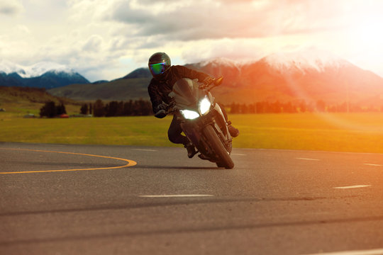 man riding sport motorcycle leaning in sharp curve with traveling scene background