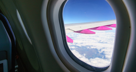 Naklejka premium Looking through aircraft window at wing, clouds and blue sky, Iceland, Europe.