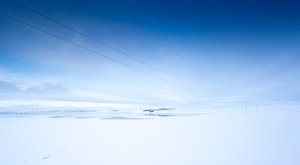 Power lines over snow covered landscape and blue sky, Iceland, Europe.