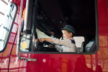 Young boy in driving seat of truck, holding steering wheel, smiling.