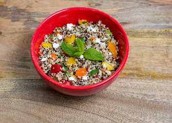 Closeup on red bowl with tri-color quinoa salad on wooden background - quinoa is a pseudograin that has all nine essential amino-acids 