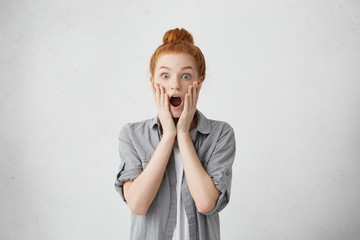 Startled ginger woman with blue eyes and freckles raising eyebrows, staring with big eyes and...