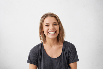 Attractive woman with short fair hair being very glad smiling with broad smile showing her perfect teeth having fun indoors. Joyful excited cheery femlae rejoicing after being proposed to marry - obrazy, fototapety, plakaty