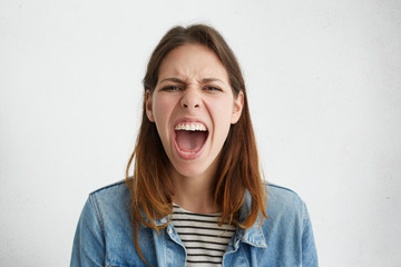 Portrait of irritated angry woman with straight dark hair frowning her face opening widely mouth expressing her dissatisfaction. Young woman in despair screaming loudly while having furious look